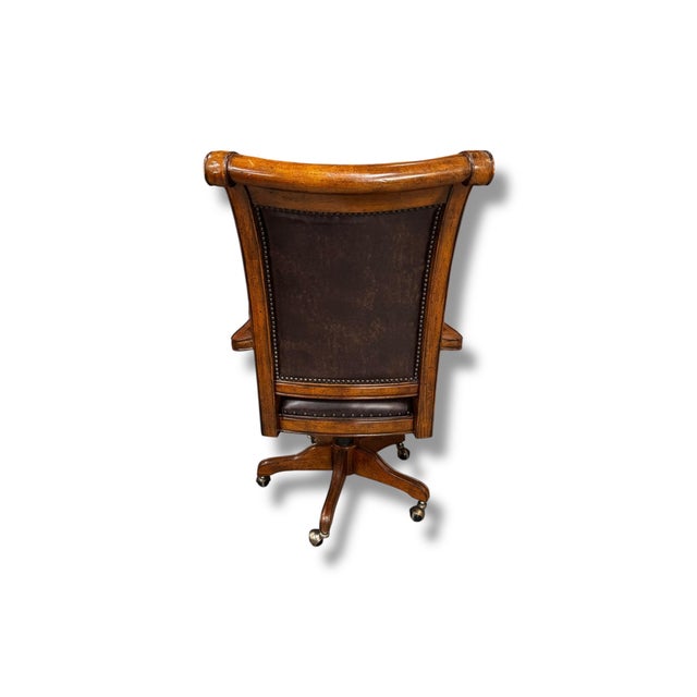 A classic wood swivel armchair featuring warm-toned wood, gracefully curved arms, and rich brown leather upholstery with...