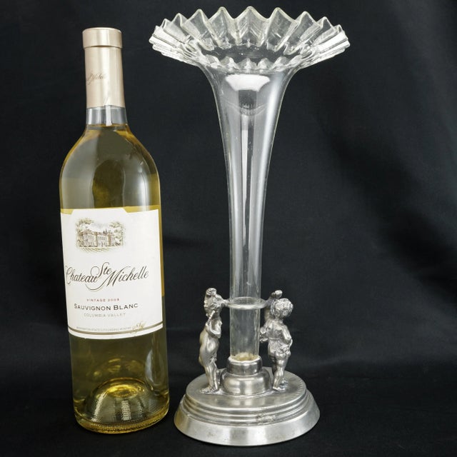 A cast pewter base with a raised platform holds a tall clear hand blown glass vase with a crimped mouth. A pair of...