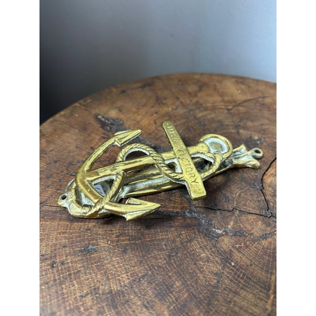 A charming vintage English brass nautical door knocker featuring a classic anchor design adorned with a banner reading HMS...