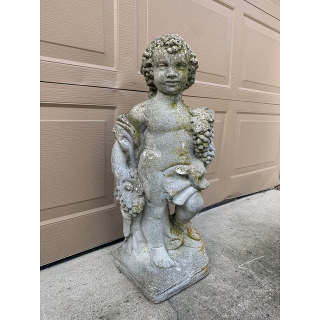 A stunning cast stone statue of a draped cherub or putti holding grapes. This allegorical statue is reminiscent of...