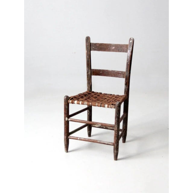 This is an antique splint weave seat chair. The rustic wooden chair features a ladder back and splint weave seat.