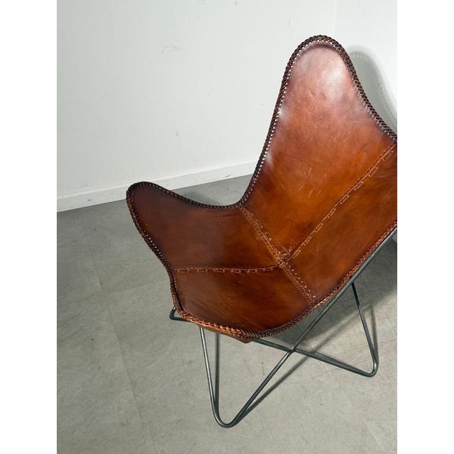 A distinctive butterfly lounge chair featuring a cognac brown leather sling seat on a slender black metal frame. Its...