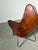 A distinctive butterfly lounge chair featuring a cognac brown leather sling seat on a slender black metal frame. Its...