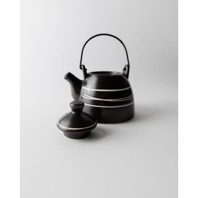 This vintage ceramic teapot from the 1980s features a striking black surface accented with fine white line detailing,...