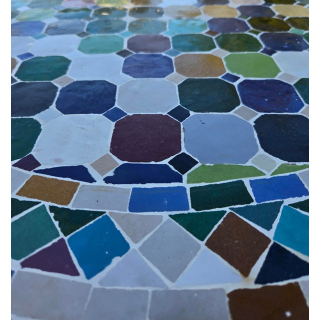 Beautiful round mosaic tile table featuring a vibrant multicolor tiled top and durable black wrought-iron style base. The...