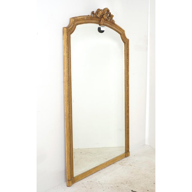 Antique French made Louis XVI style mirror with an arched crest and ribbon motif. The frame with fluted molding has a gold...