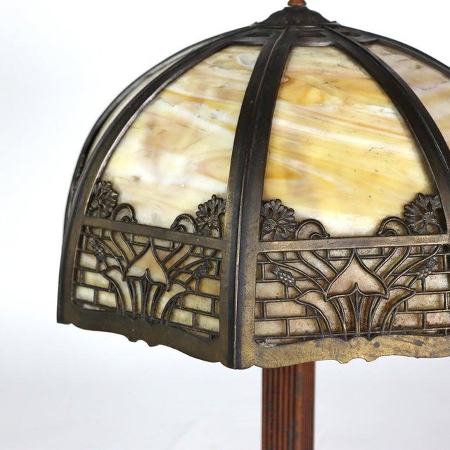 This antique table lamp, in the manner of Bradley & Hubbard, features an 8-panel slag glass shade with intricate overlay...