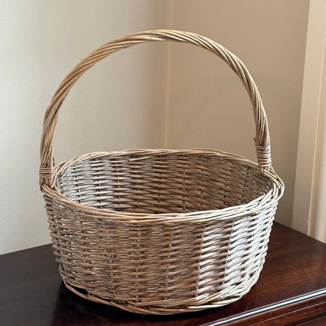 A beautifully handwoven vintage willow gathering basket featuring a generous round form and a gracefully arched wrapped...