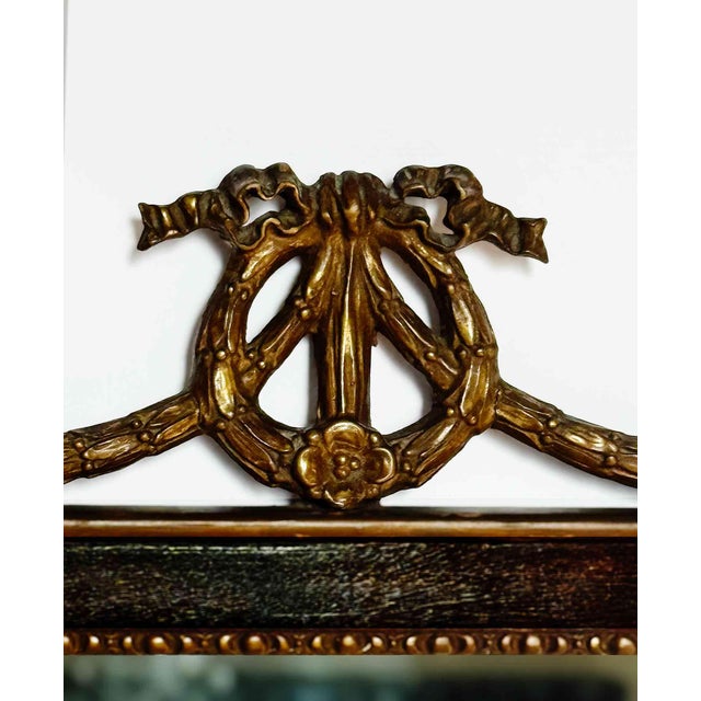 Antique French Louis XVI-style mirror features a rich wood frame accented with ornate, hand-carved parcel-gilt...