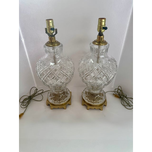 A matching pair of neoclassical urn-form table lamps with diamond-pattern glass bodies, fluted necks, and faceted pedestal...