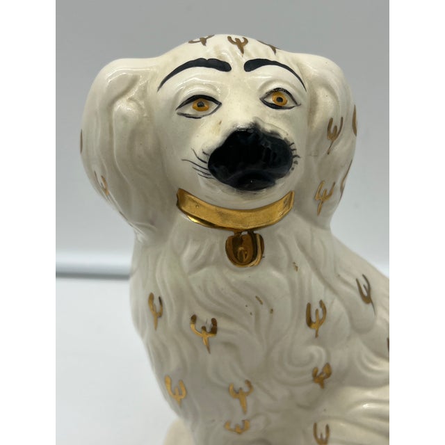 Antique Beswick Spaniel featuring a white glaze adorned with golden accents and hand-painted details. The piece depicts a...