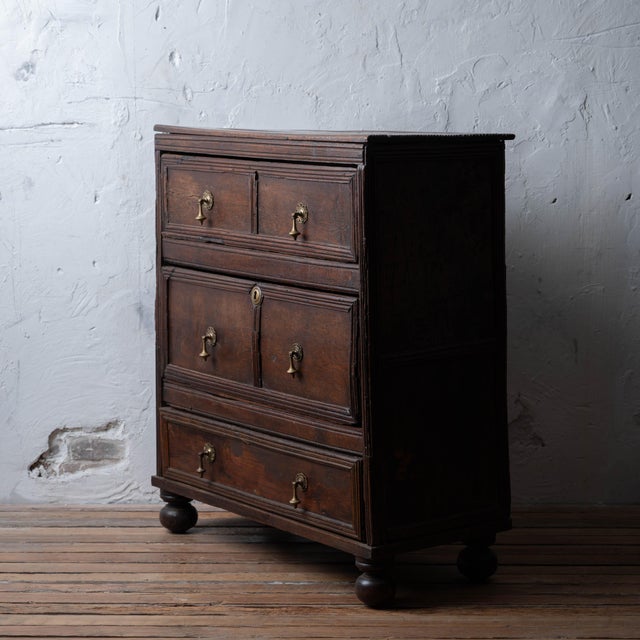 An English Jacobean oak chest of drawers with a dark aged finish, beaded mouldings to the drawer fronts, and turned bun...