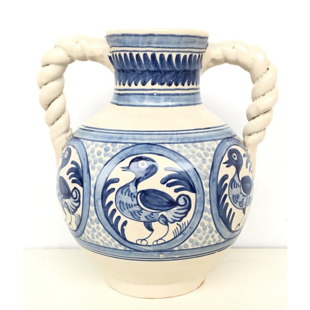 About A striking Spanish glazed earthenware two-handled blue and white painted urn with foliate molded handles, the body...