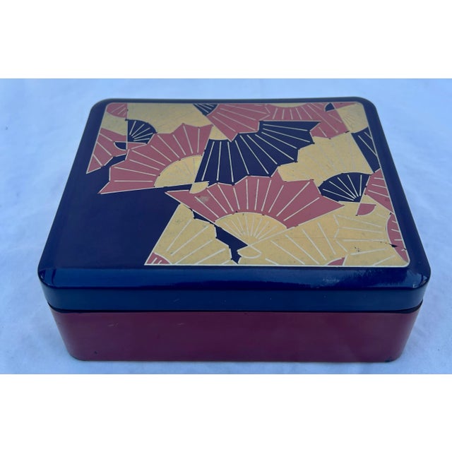 Vintage Chinoiserie inspired two tone lacquered box. The purple lid is decorated with Japanese fans in peach, rose, and...