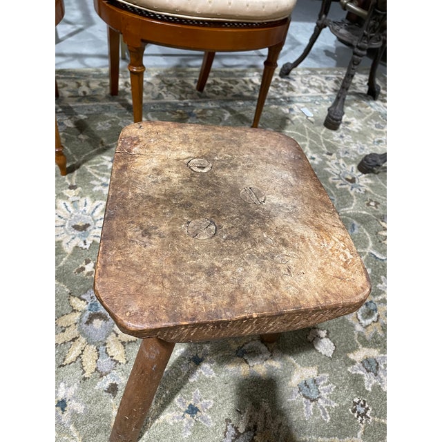This is an authentic antique rustic three-legged milking stool, hand-crafted with a thick, irregular wood seat and splayed...
