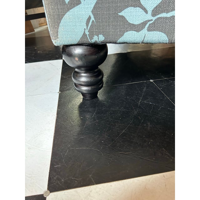 An ottoman with wood turned legs and upholstered in a whimsical flora and fauna printed fabric.