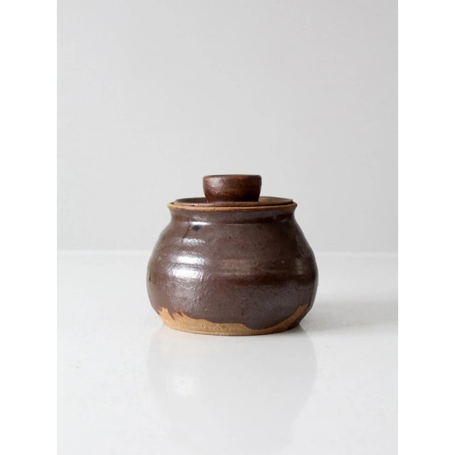 This is a vintage studio pottery jar. Signed by the artist, the hand-crafted jar features a deep brown glaze. It has an...