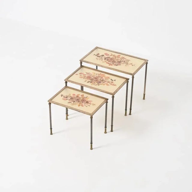This decorative set of 3 brass nesting tables can be dated in the 1960s. The resin table tops are filled with dried...