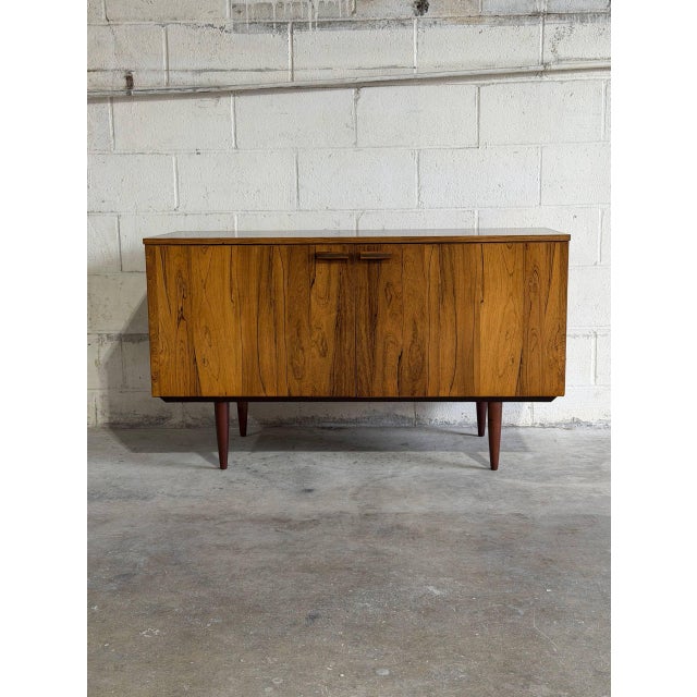 This minimalist low-profile credenza features a streamlined rectangular frame supported by dark tapered legs. The double...