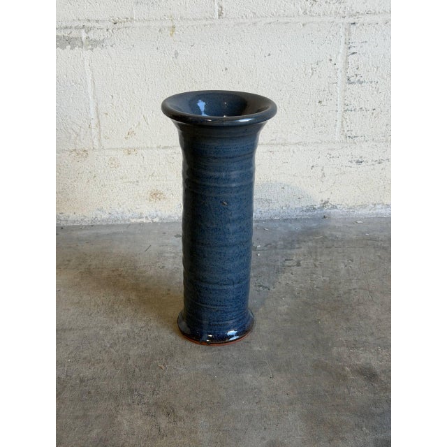 This commanding tall cylinder studio pottery vase features a richly variegated, mottled blue glaze that flows over a...