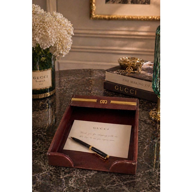 Gucci desk tray dating to the 1970s, covered in deep red leather and accented with gold-toned metal hardware. The...