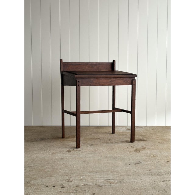 Early oak schoolhouse writing desk with a hinged slant-front lid and open interior storage beneath. Built with the simple,...