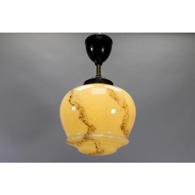 Small-scale german art deco pendant light in marbled ivory color glass with warm ambient illumination and bakelite...