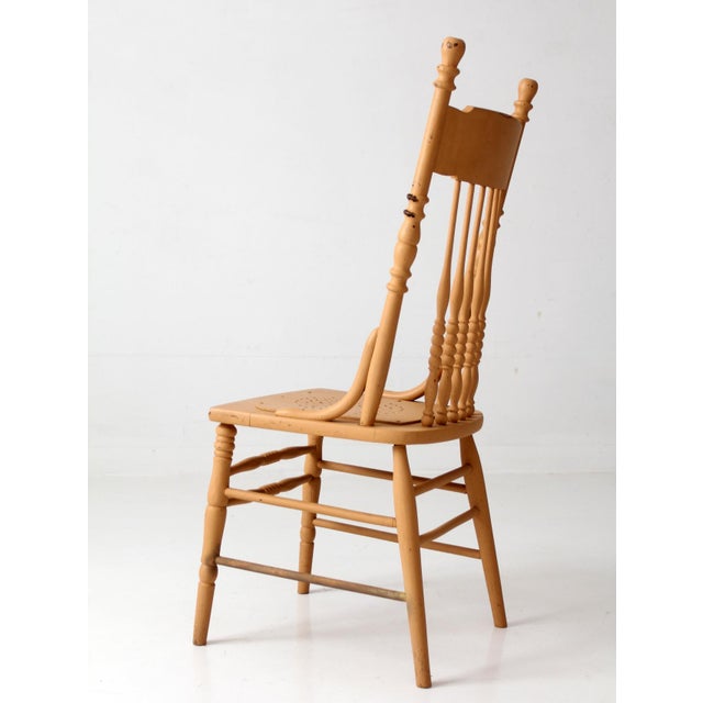 Antique pressback chair with a tall spindle back, turned details, and a pressed floral motif across the crest rail....