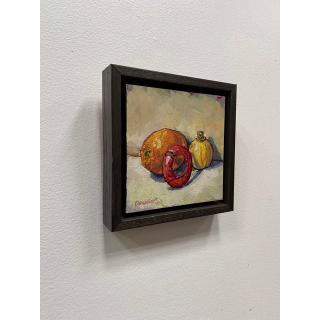 This oil on board artwork features a vibrant arrangement of an orange, a lime, and a decorative can, presented with a...