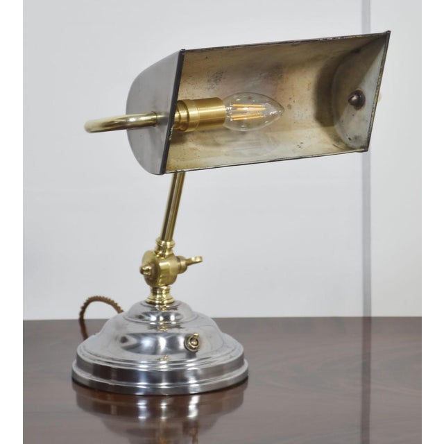Adjustable Bankers desk lamp, the silvered circular stepped base and brass pivoted sweeping arm supporting adjustable...