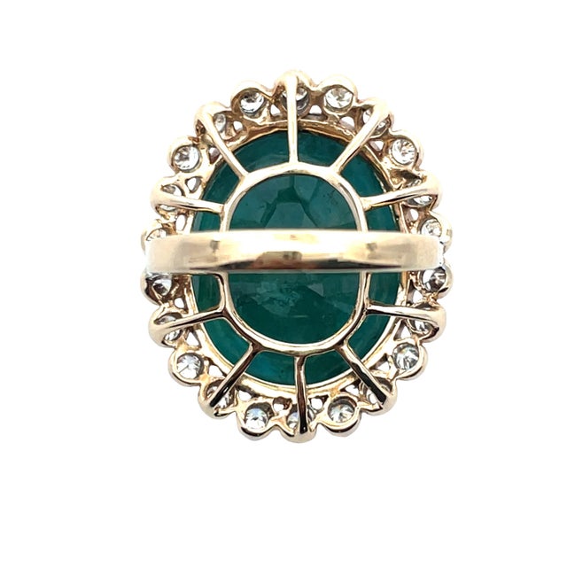 14K gold statement ring featuring a striking 23.36-carat oval-cut green emerald, encircled by 1.21 carats of round-cut...