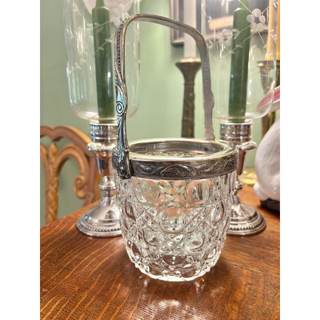 This vintage cut crystal ice bucket dates to approximately the 1930s–1940s, and features decorative silver-plated mounts...