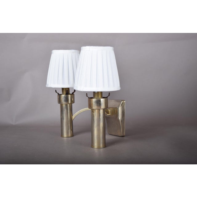 Single modernist two-light wall sconce in brass-toned metal. A shaped rectangular backplate and arched arm carry two...