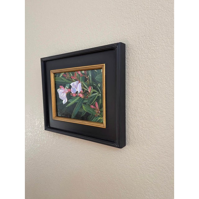 This oil on board painting depicts vibrant oleander flowers amidst lush green foliage, capturing their delicate petals in...