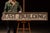 Long, hand-painted wooden directional sign reading "EAST BUILDING," rendered in bold block lettering over a heavily...