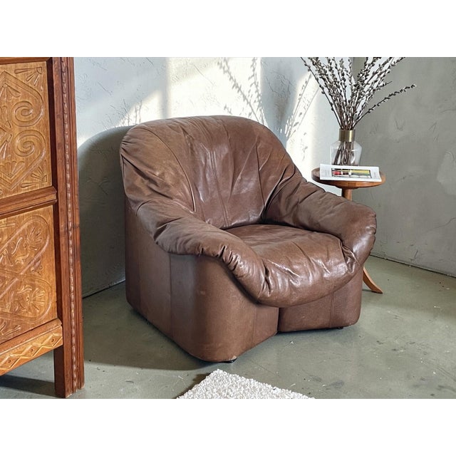A beautifully shaped vintage lounge chair from the 1970s, upholstered in rich brown leather. The chair features a soft,...