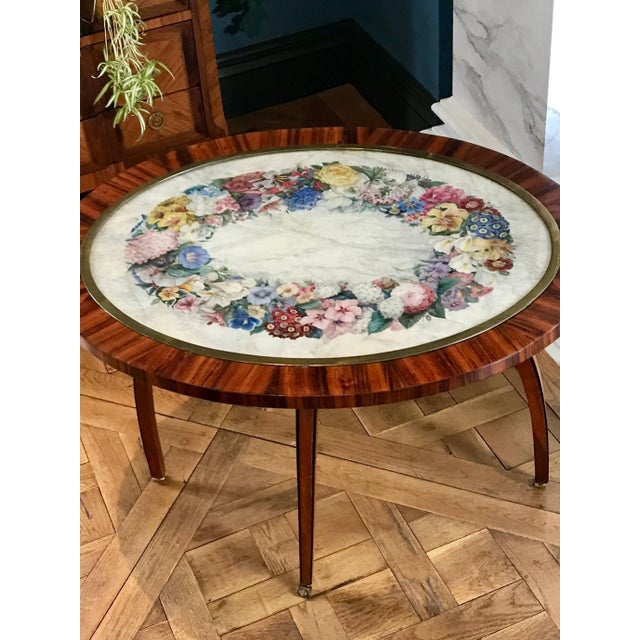 This beautiful kingwood side table has a hand-painted floral wreath and is protected under a glass and is framed in brass.