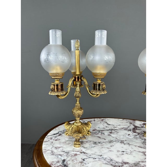 An elegant pair of three-light decorative candelabras, richly adorned with embossed plant and foliage motifs. Each...