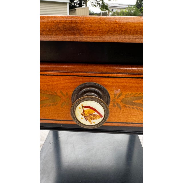 Charming vintage Hitchcock-style side table featuring a warm wood top with delicate floral stenciling, contrasting black...