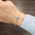 This elegant bangle bracelet embodies a sleek and modern design. At its center, a natural emerald-cut blue sapphire...