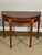 An English George III demilune table featuring a solid figured mahogany top with satinwood pilasters and banding, framed...