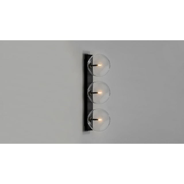 Oslo triple sconce Three glass bubbles alight upon a slender rectangle of brass for an essential design. Inspired by the...