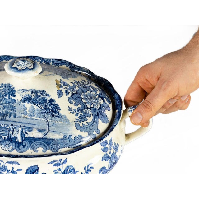 A blue and white earthenware tureen made in Staffordshire, England, in the early 20th century. It features a countryside...