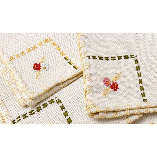 A charming set of four vintage hand-embroidered linen napkins featuring delicate floral bouquets, hand-stitched drawn-...