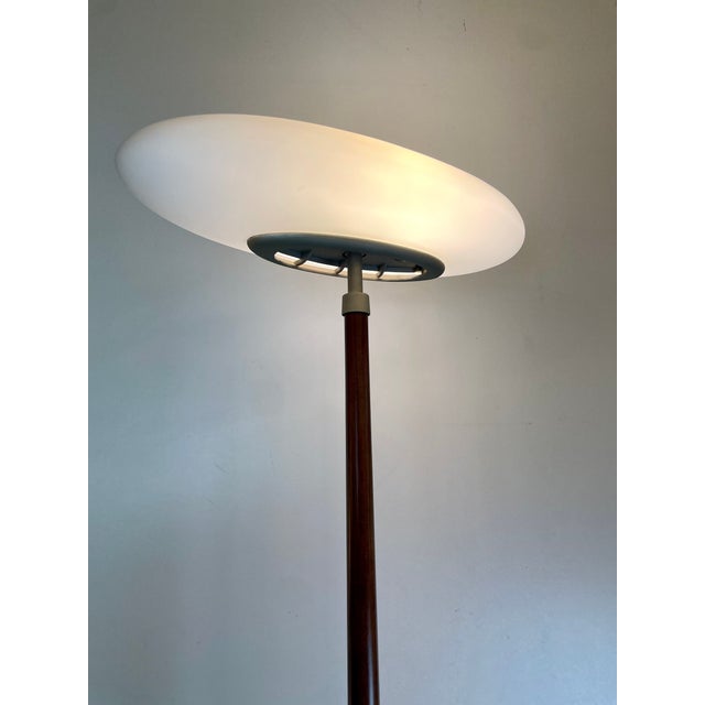 Pao, tall floor lamp made with a satin glass base, ebonized wood stem, and an opal glass oval-shaped diffuser that emits a...