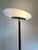 Pao, tall floor lamp made with a satin glass base, ebonized wood stem, and an opal glass oval-shaped diffuser that emits a...