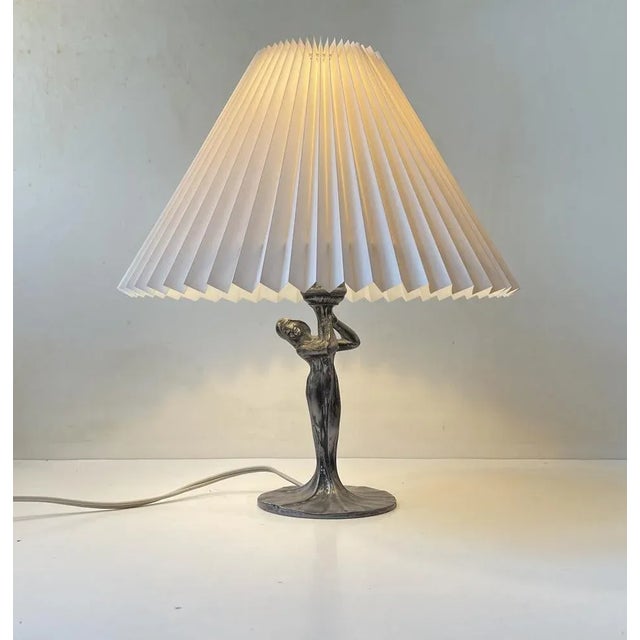 I the style of Max Le Verrier comes this stylized table lamp in patinated pewter. It depicts a woman whos dress floats...