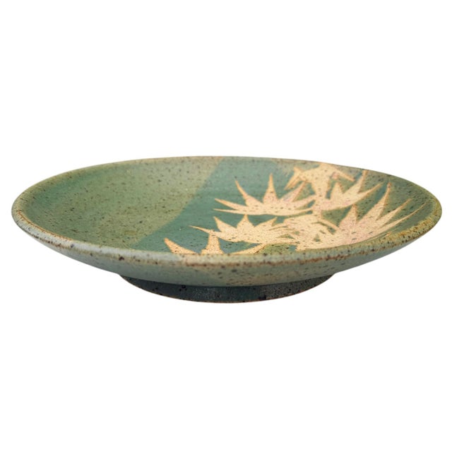 Hand-thrown contemporary studio stoneware bowl featuring a soft moss green speckled glaze with a carved Bird of Paradise...