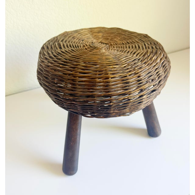 A vintage tripod wicker stool, attributed to Tony Paul, Circa 1950s. Stout, tapered, angled maple legs give support to the...