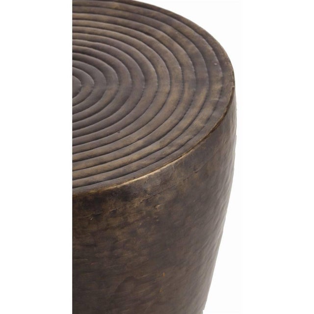 This iron drum shaped side table features an antique bronze finish and repousse ringed detail on the top surface....